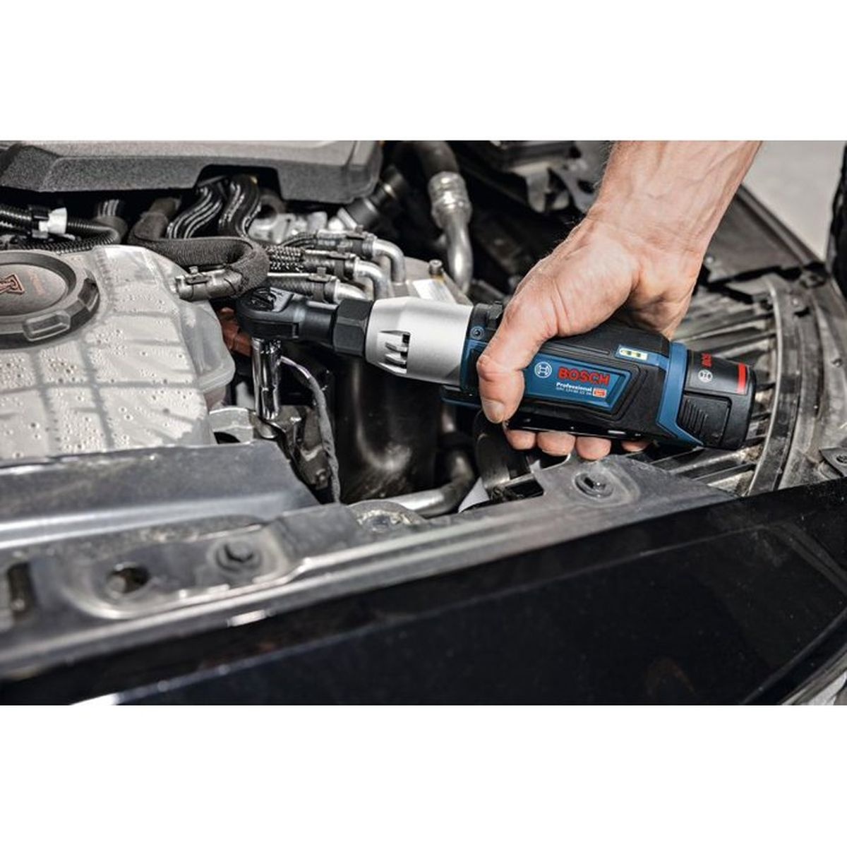Eine Person benutzt eine blau-silberne Bosch Akku-Ratsche an einem Automotor.