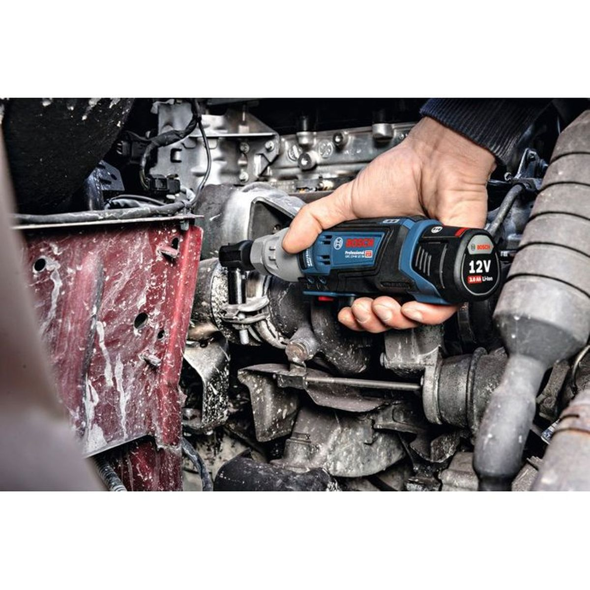 Eine Hand hält eine blaue Bosch 12V Akku-Ratsche im Motorraum.