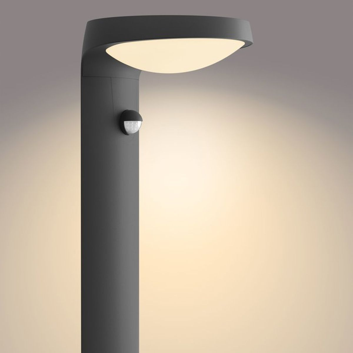 Una moderna lampada da esterno grigio scuro con sensore e luce calda su sfondo neutro.