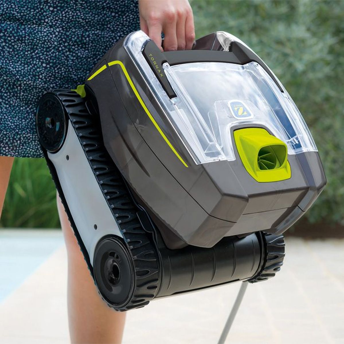 Eine Hand hält einen grauen und grünen Poolroboter mit großen schwarzen Kettenrädern.