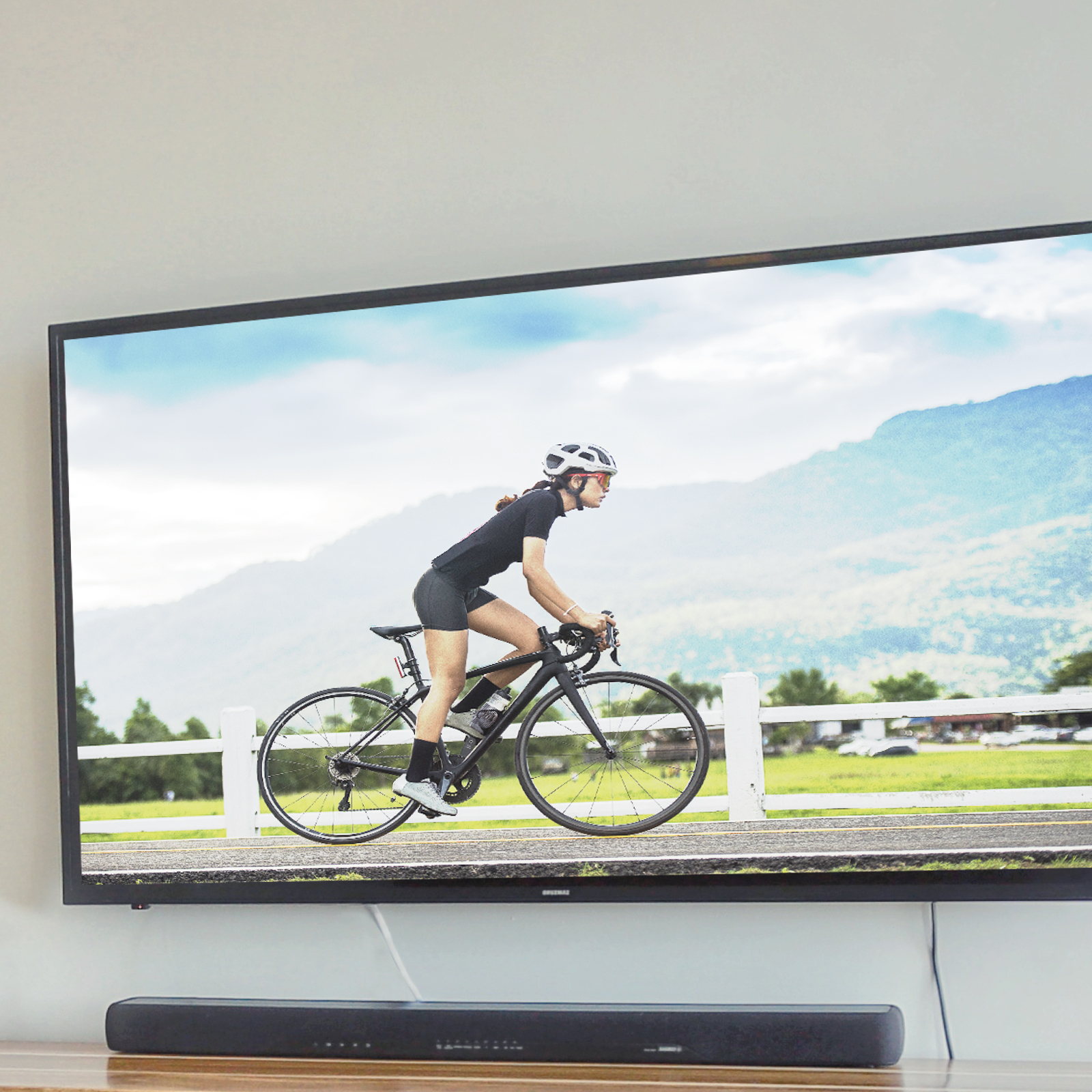 Una televisione mostra una ciclista che pedala su una strada asfaltata con sfondo montano.
