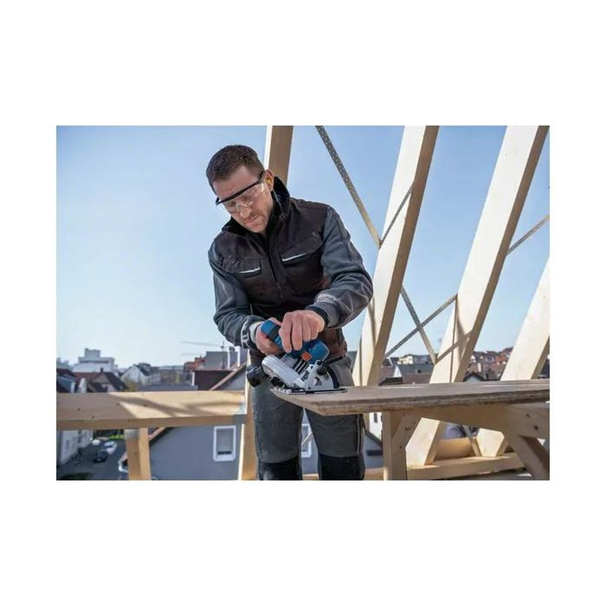 Un trabajador con gafas de protección usa una sierra circular en una tabla de madera al aire libre.