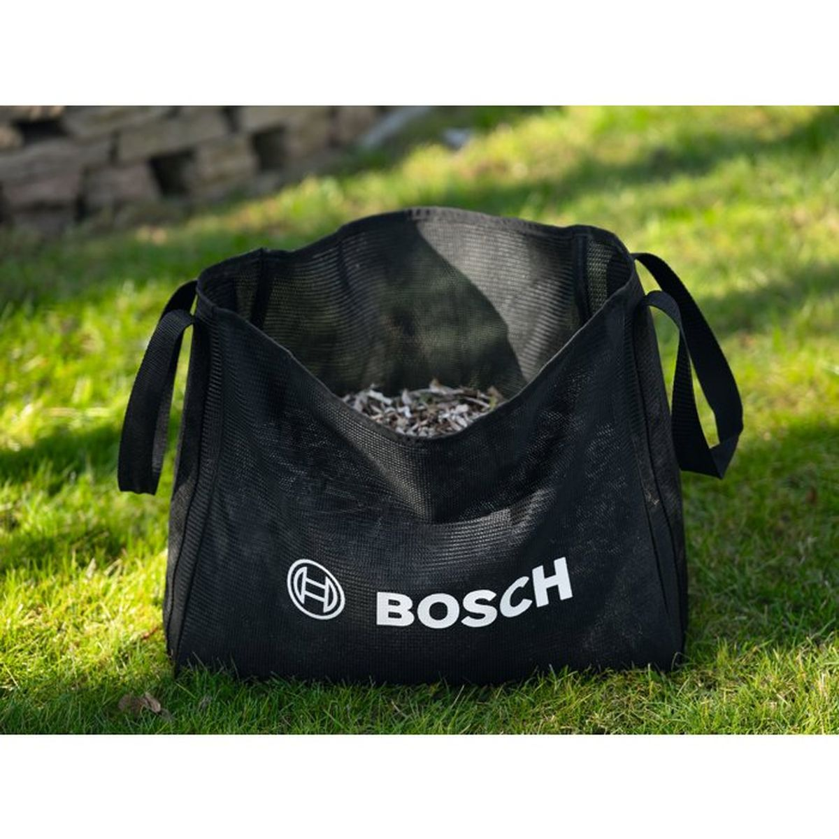 Ein schwarzer Bosch Gartensack mit Griffen auf grünem Rasen.
