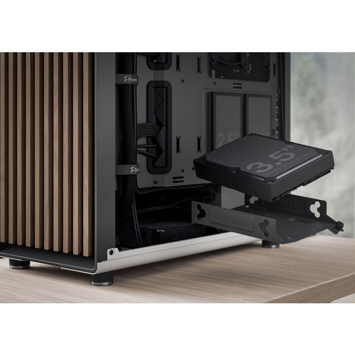 A 3.5-inch hard drive is inserted into a drive cage of a wooden PC case on a wooden desk.