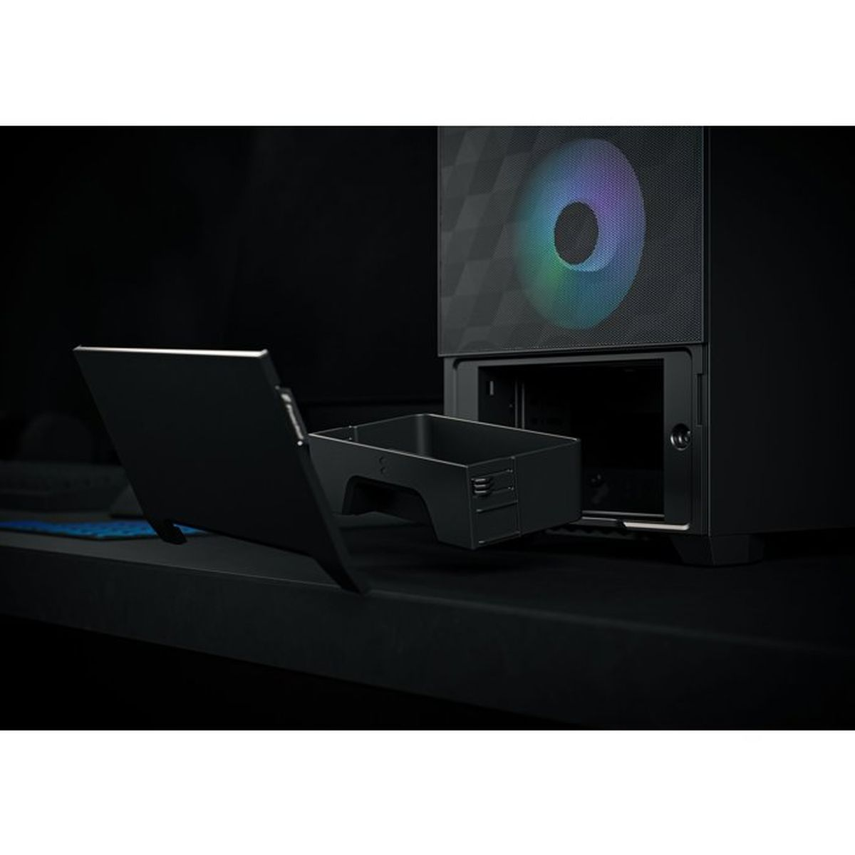 Ein schwarzes PC-Gehäuse auf einem Schreibtisch mit einer herausziehbaren Schublade und einem regenbogenfarben leuchtenden Frontlüfter.