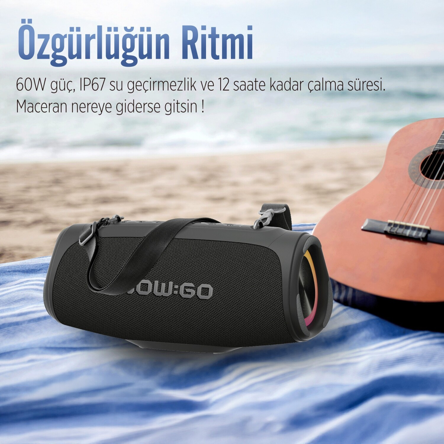 Czarny głośnik przenośny i gitara akustyczna na niebieskim ręczniku na plaży.