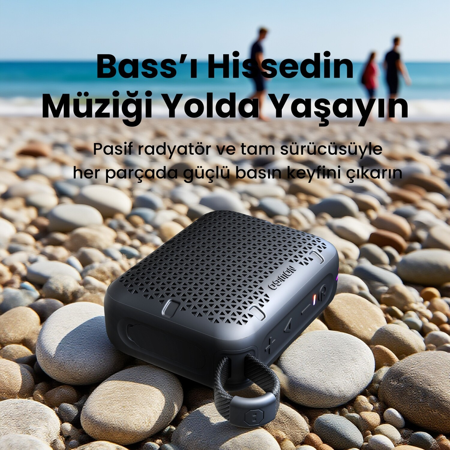 Czarny głośnik Bluetooth spoczywa na kamienistej plaży przed niebieskim morzem.