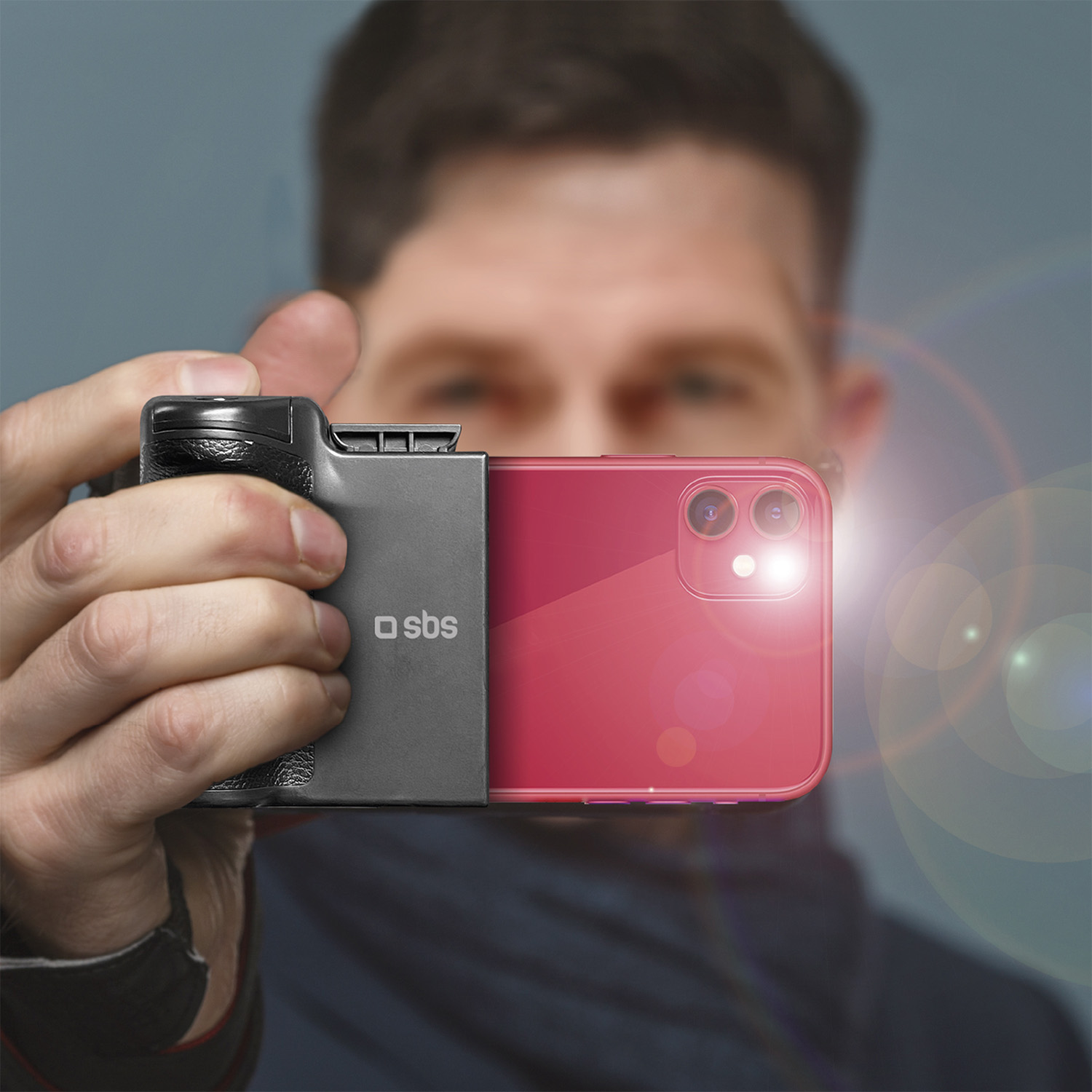 Un hombre sostiene un smartphone rojo con empuñadura de cámara negra, simulando una cámara.