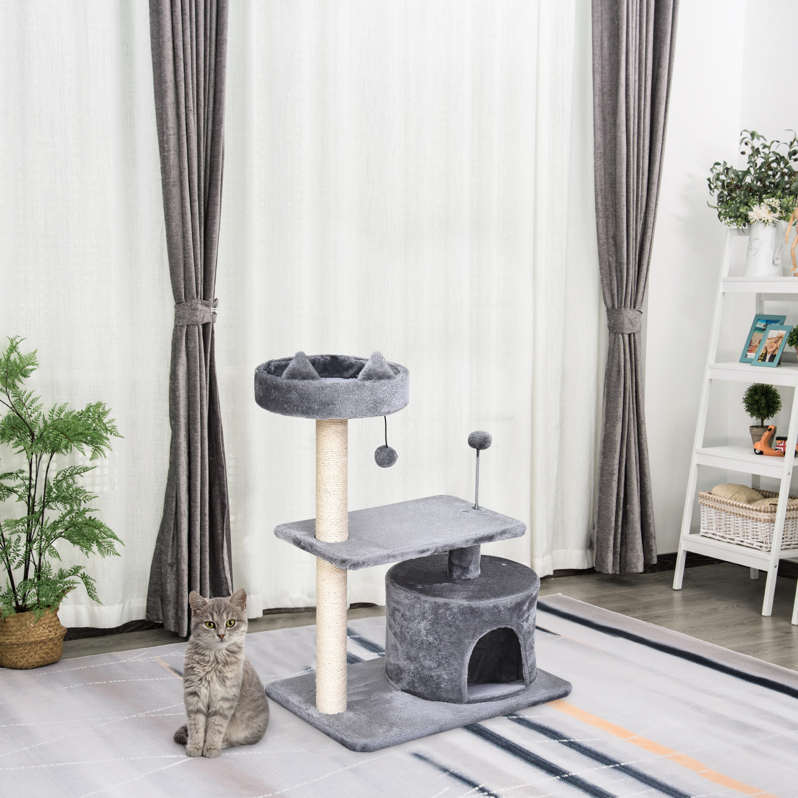 Un gato gris se sienta junto a un rascador gris a juego sobre una alfombra estampada en una habitación luminosa.