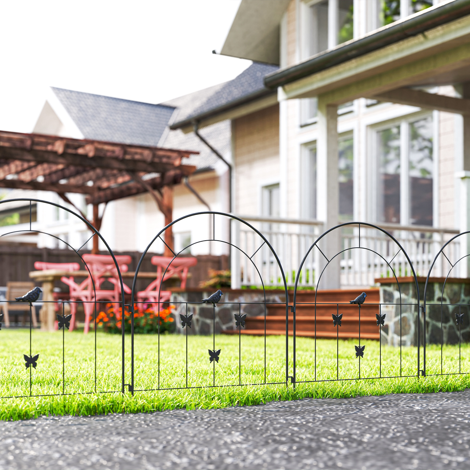 Una valla de jardín de metal negro con decoraciones de mariposas y aves en un césped verde frente a una casa.