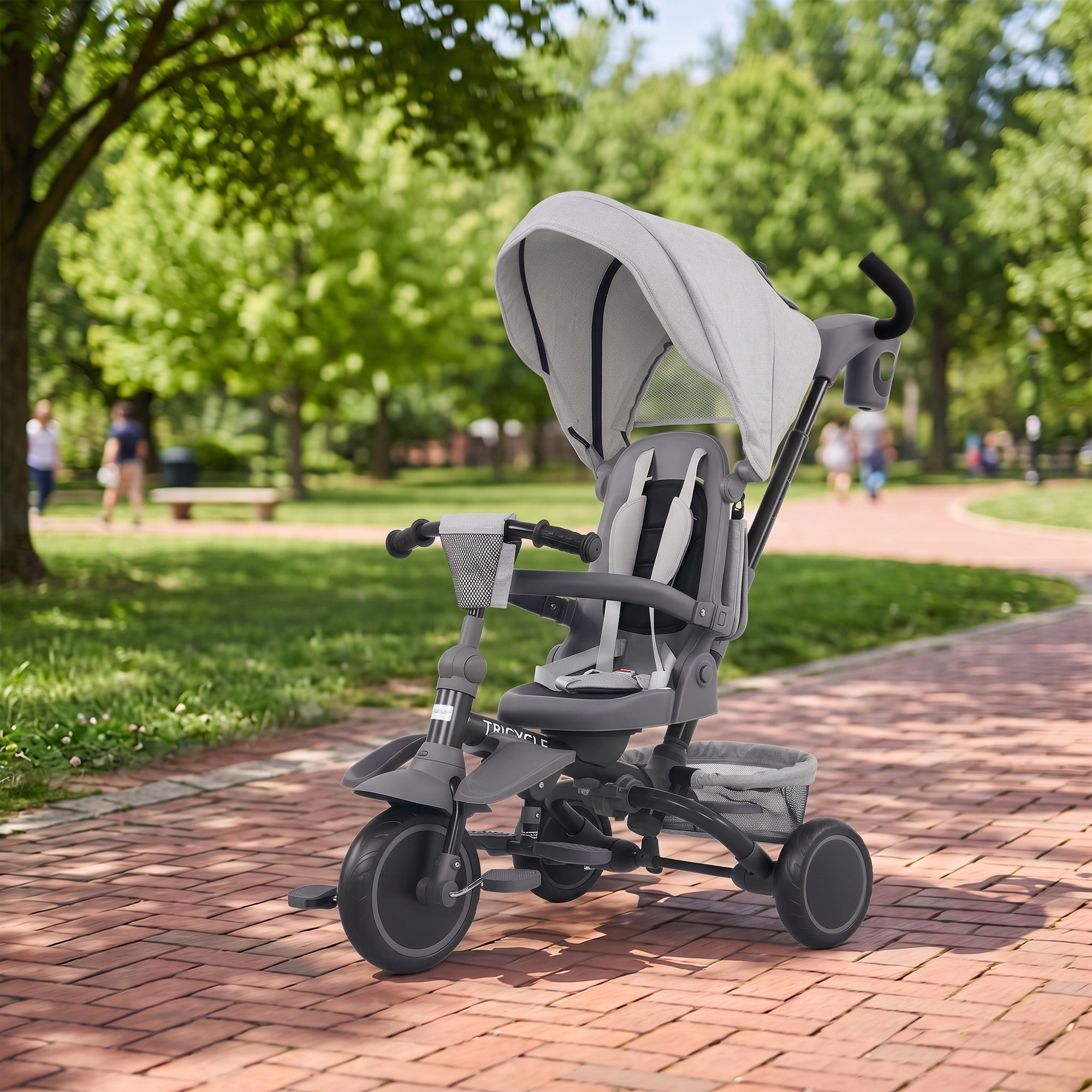 Un triciclo infantil gris con capota se encuentra en un camino de ladrillos en un parque.