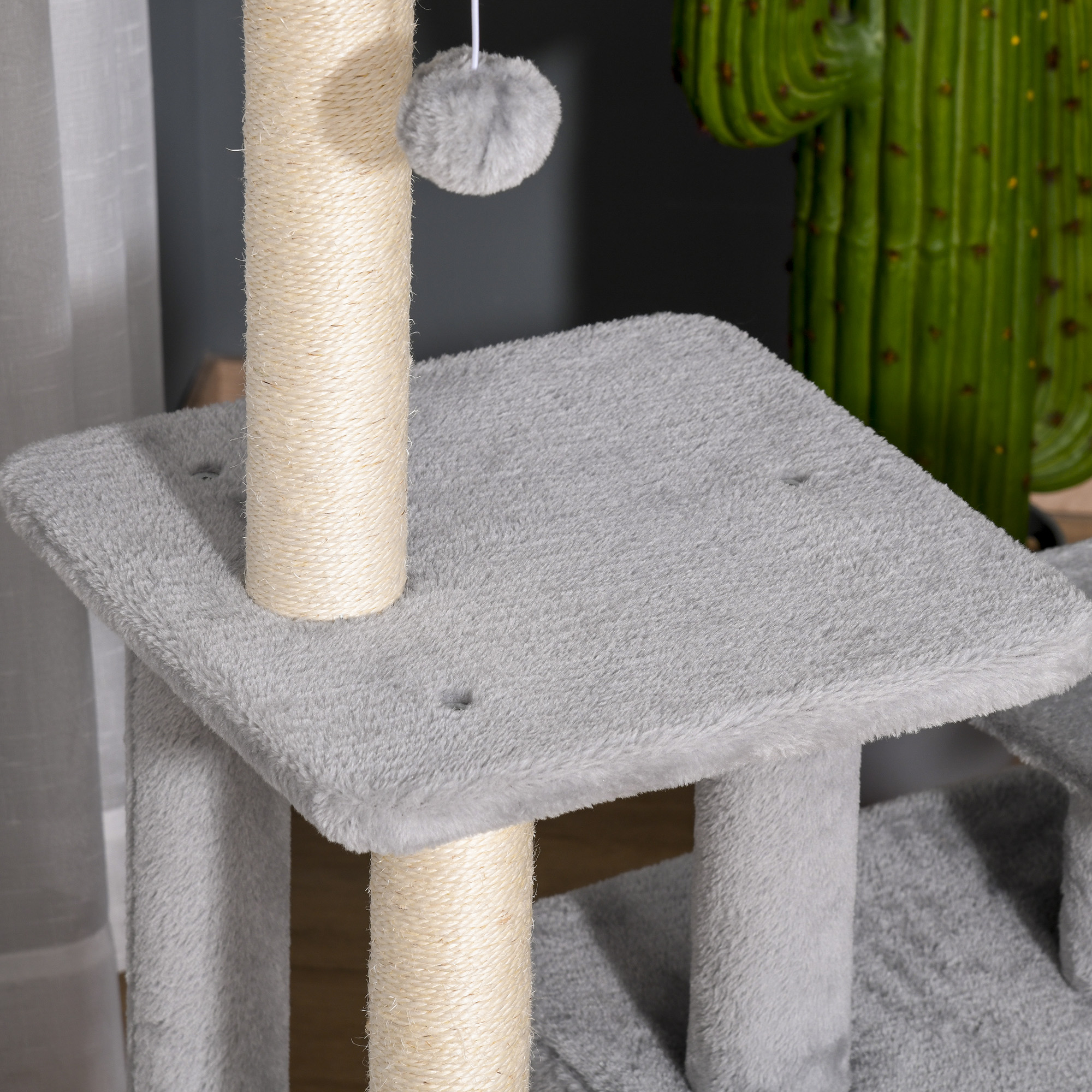 Árbol para gatos gris con postes de sisal, una pelota colgante y un cactus artificial al fondo.