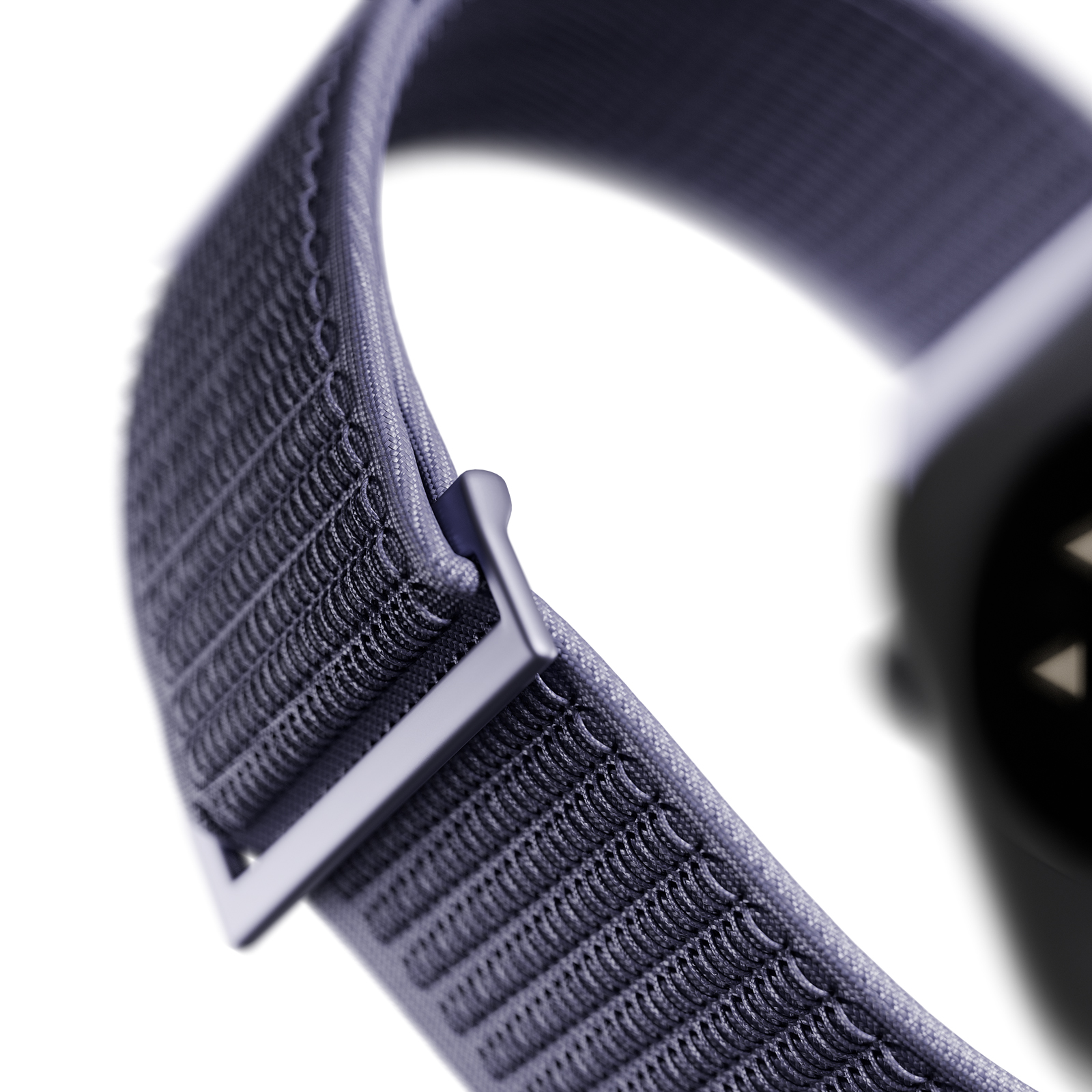 Primer plano de una correa de reloj textil gris con hebilla metálica cuadrada y reloj borroso al fondo.