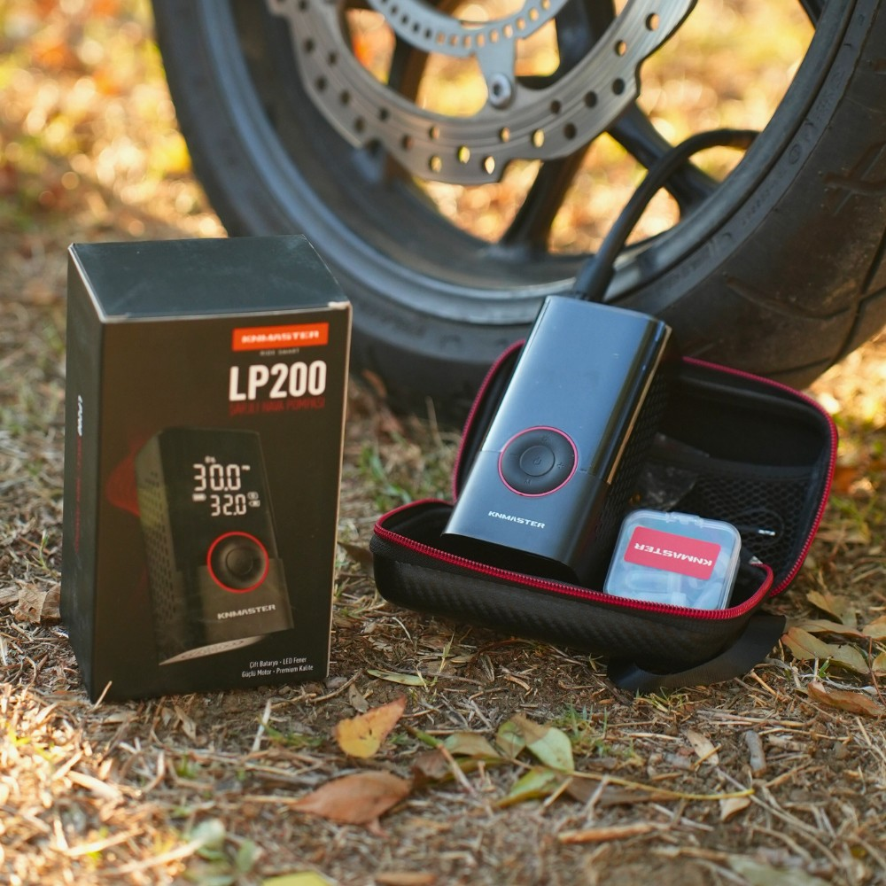 Çimler üzerinde bir motosiklet lastiğinin önünde kutulu siyah LP200 hava pompası.