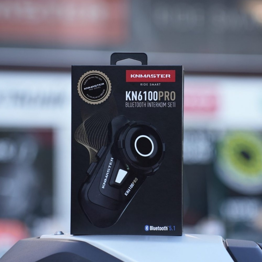 Beyaz yüzey üzerinde duran Knmaster KN6100PRO Bluetooth interkom setinin siyah kutusu.