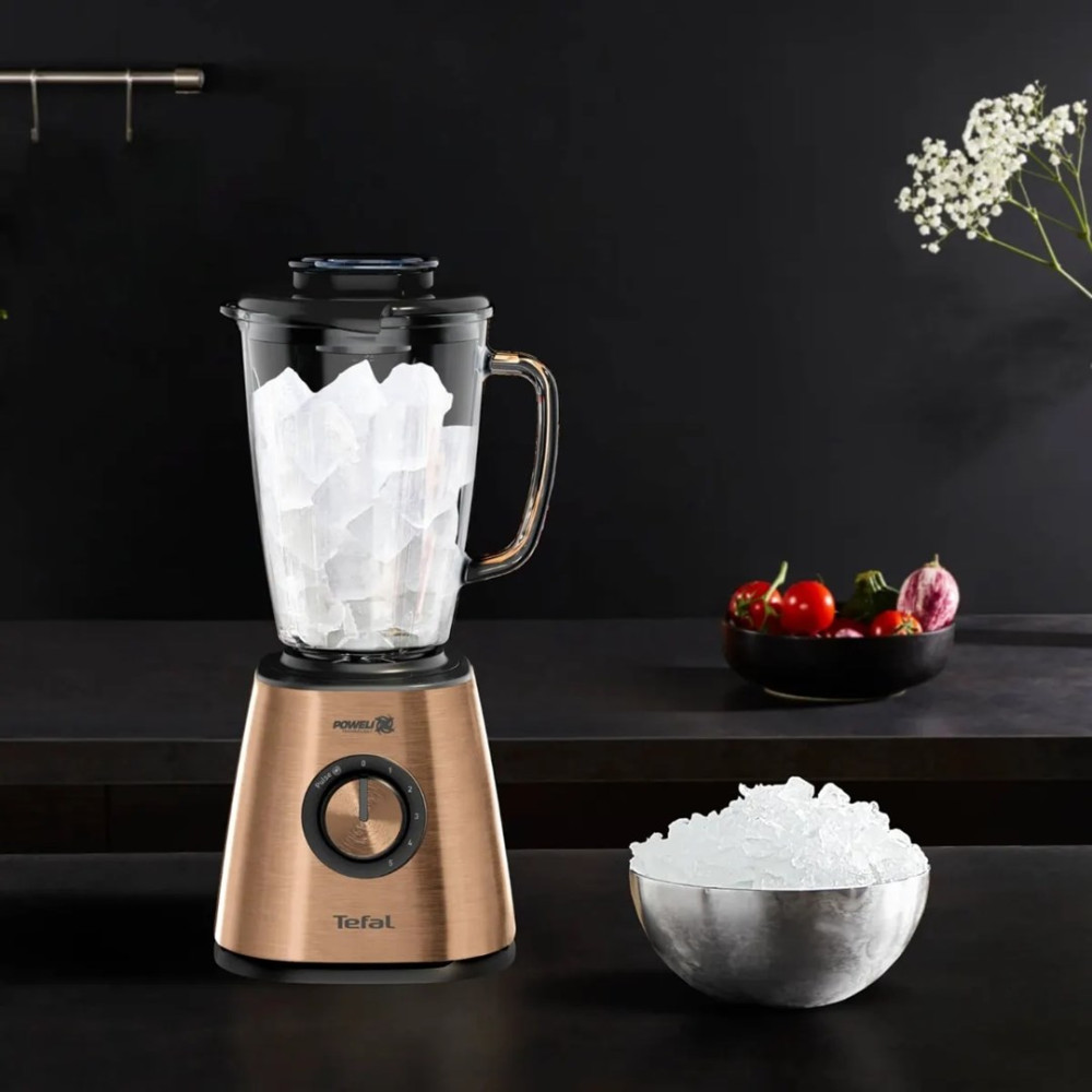 Różowozłoty blender Tefal wypełniony kostkami lodu na ciemnym blacie, obok miski z kruszonym lodem.