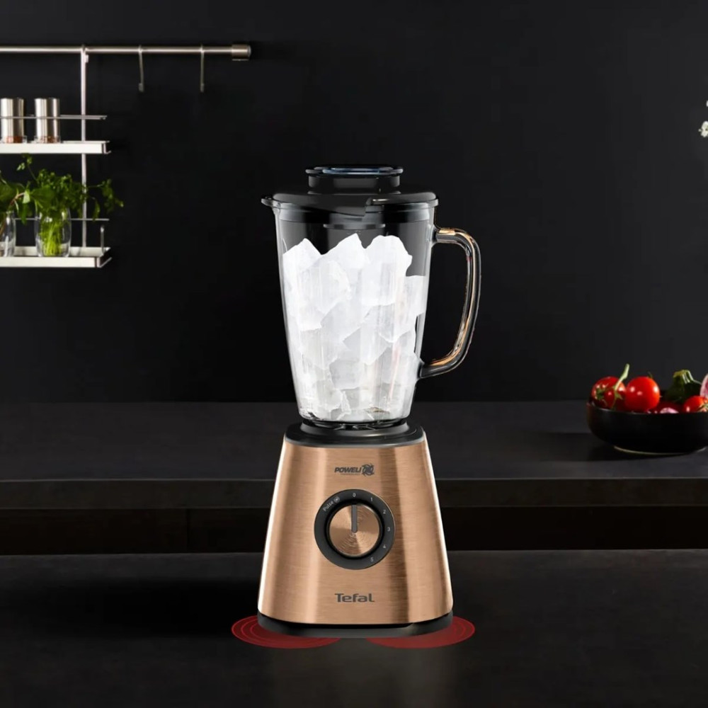 Blender Tefal z miedzianą podstawą wypełniony kostkami lodu stoi na ciemnym blacie kuchennym.