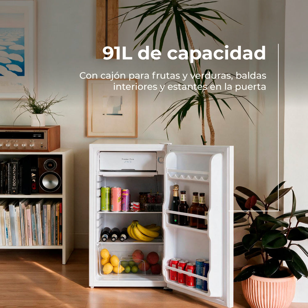 Pequeño frigorífico blanco con puerta abierta, lleno de bebidas y frutas, en un salón luminoso.
