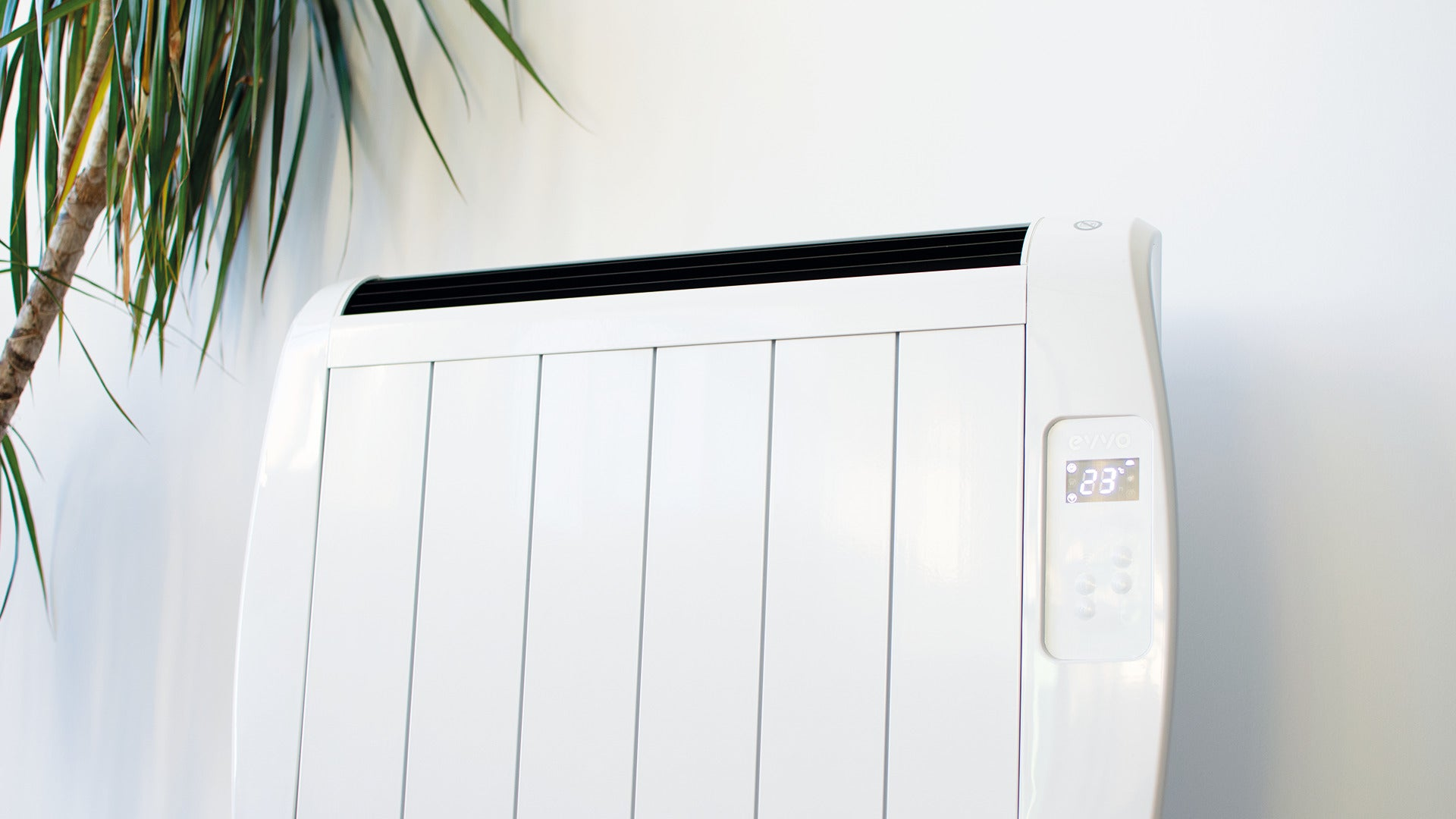 Un radiador eléctrico blanco con pantalla digital en una pared, con una planta al lado.
