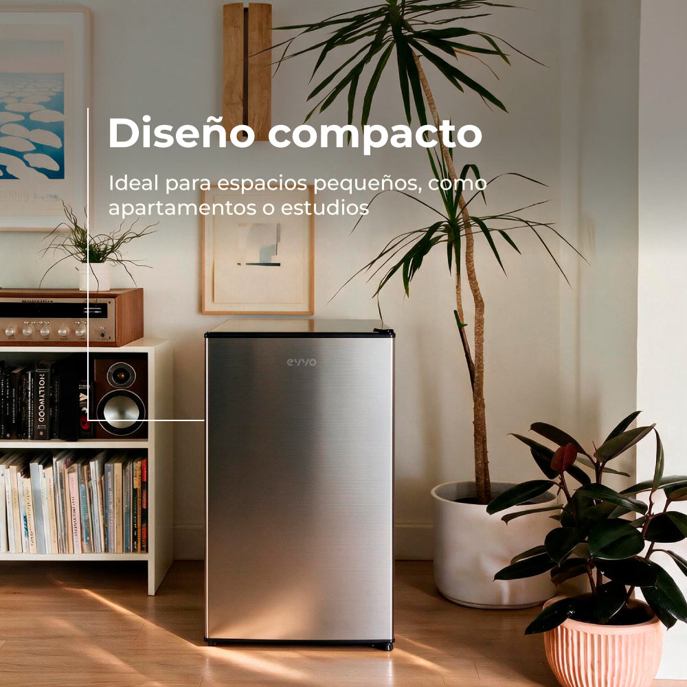 Nevera plateada compacta en una sala con plantas y estantería.