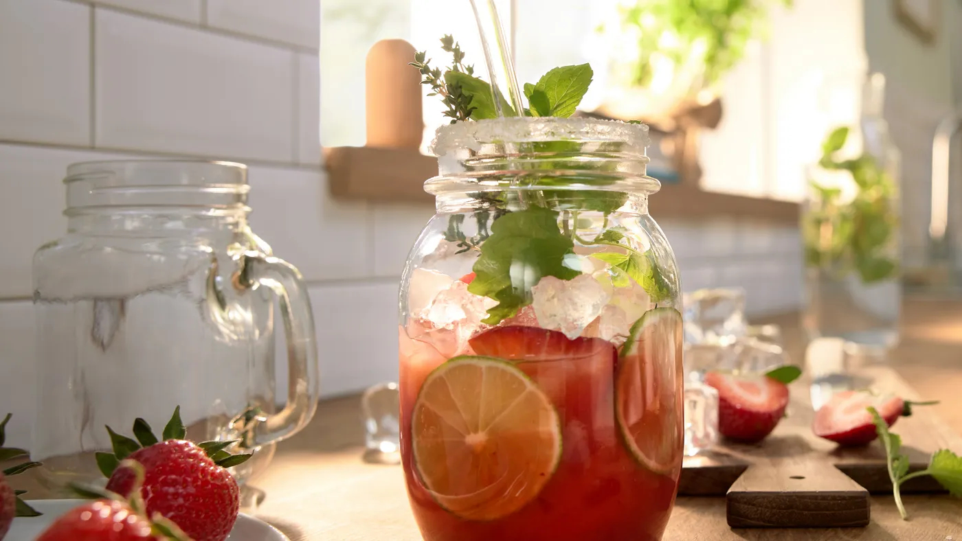 Una rinfrescante bevanda rossa con fette di lime, ghiaccio, menta e fragole in un barattolo su un bancone.