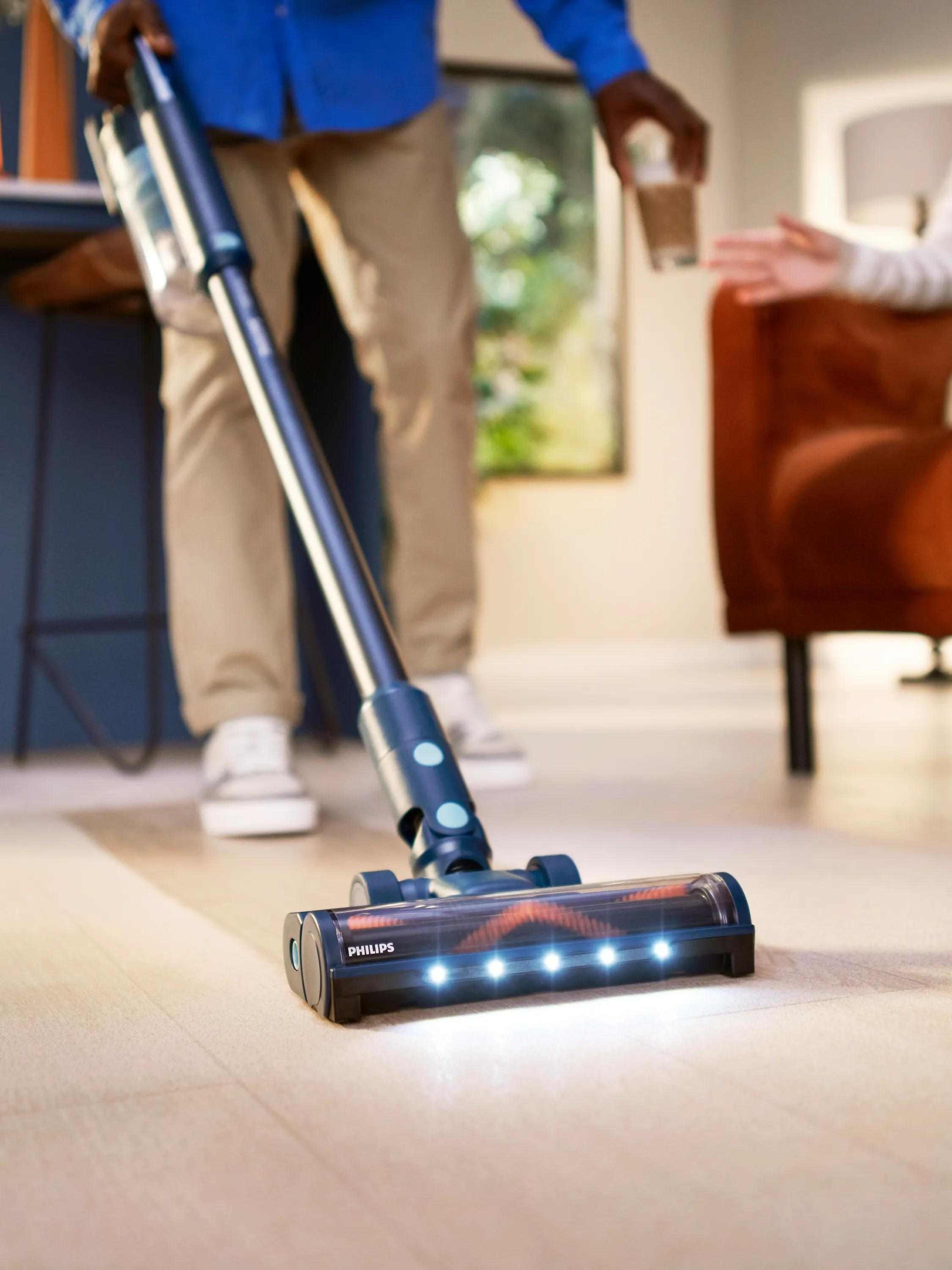 Mężczyzna używa niebieskiego odkurzacza Philips z oświetleniem LED na jasnej podłodze.
