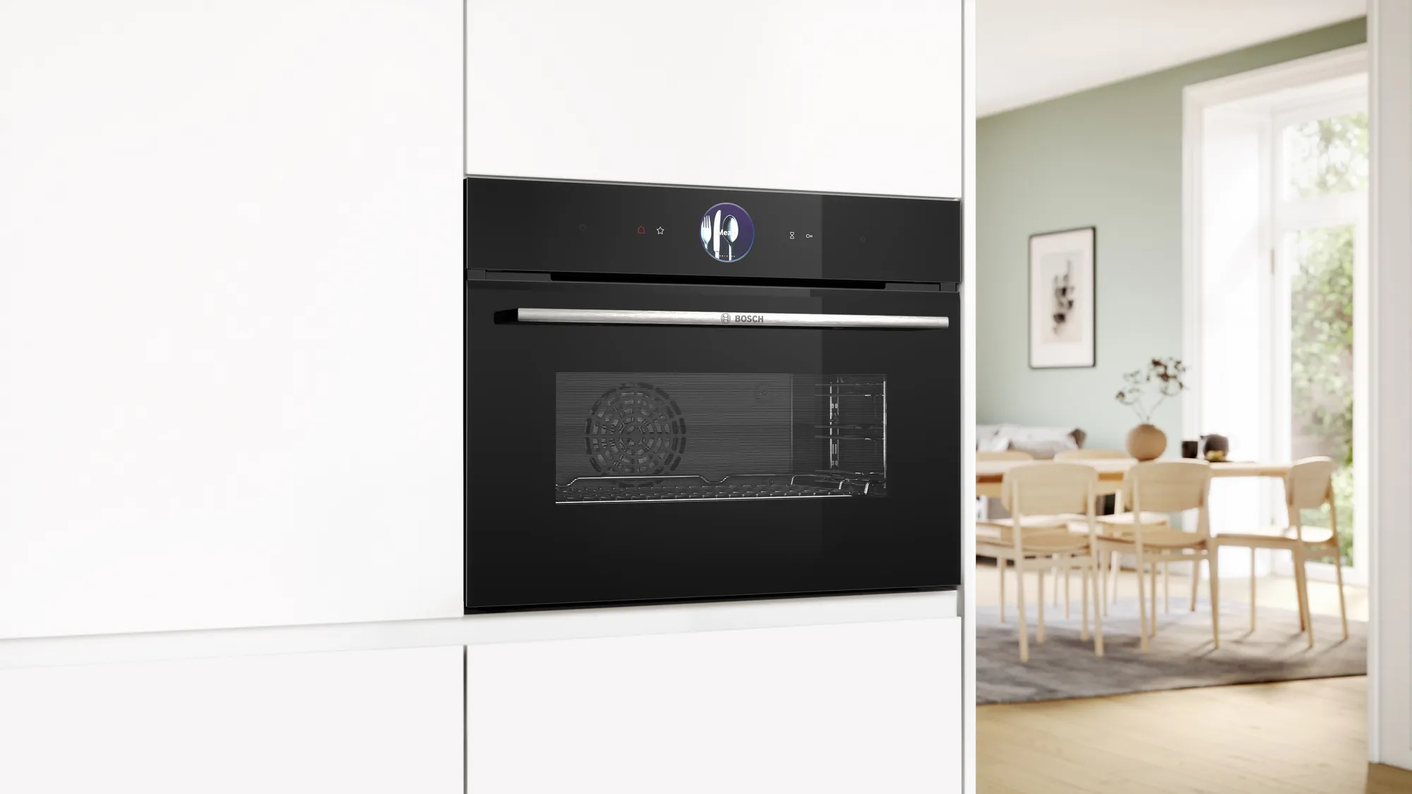 Un forno da incasso Bosch nero in una cucina bianca, con una zona pranzo luminosa sullo sfondo.