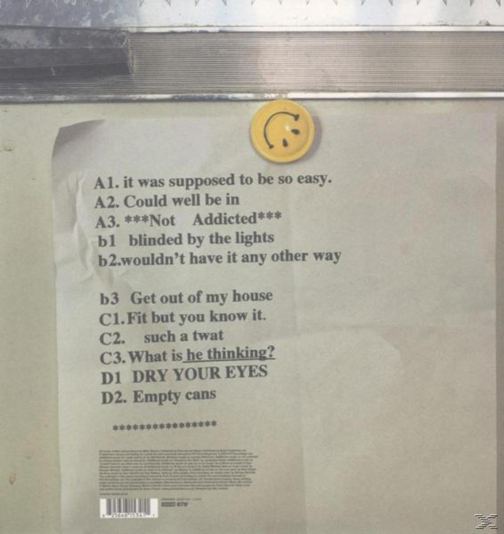 Papierblatt mit gedruckten Liedtexten und einem gelben Smiley-Magneten an einer Wand.