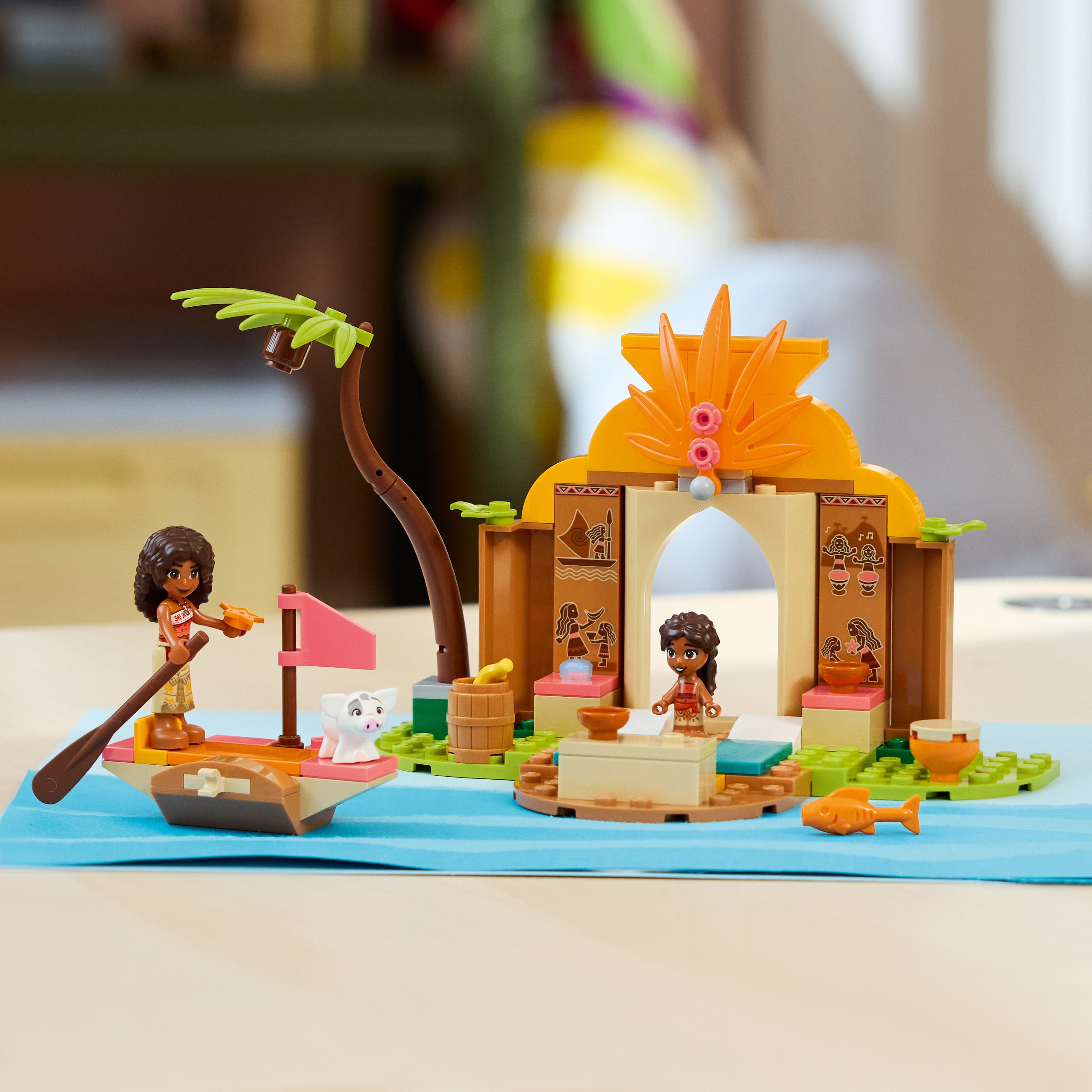 Set de Lego con Moana en una canoa con un cerdo, una palmera y un templo colorido sobre una base azul.