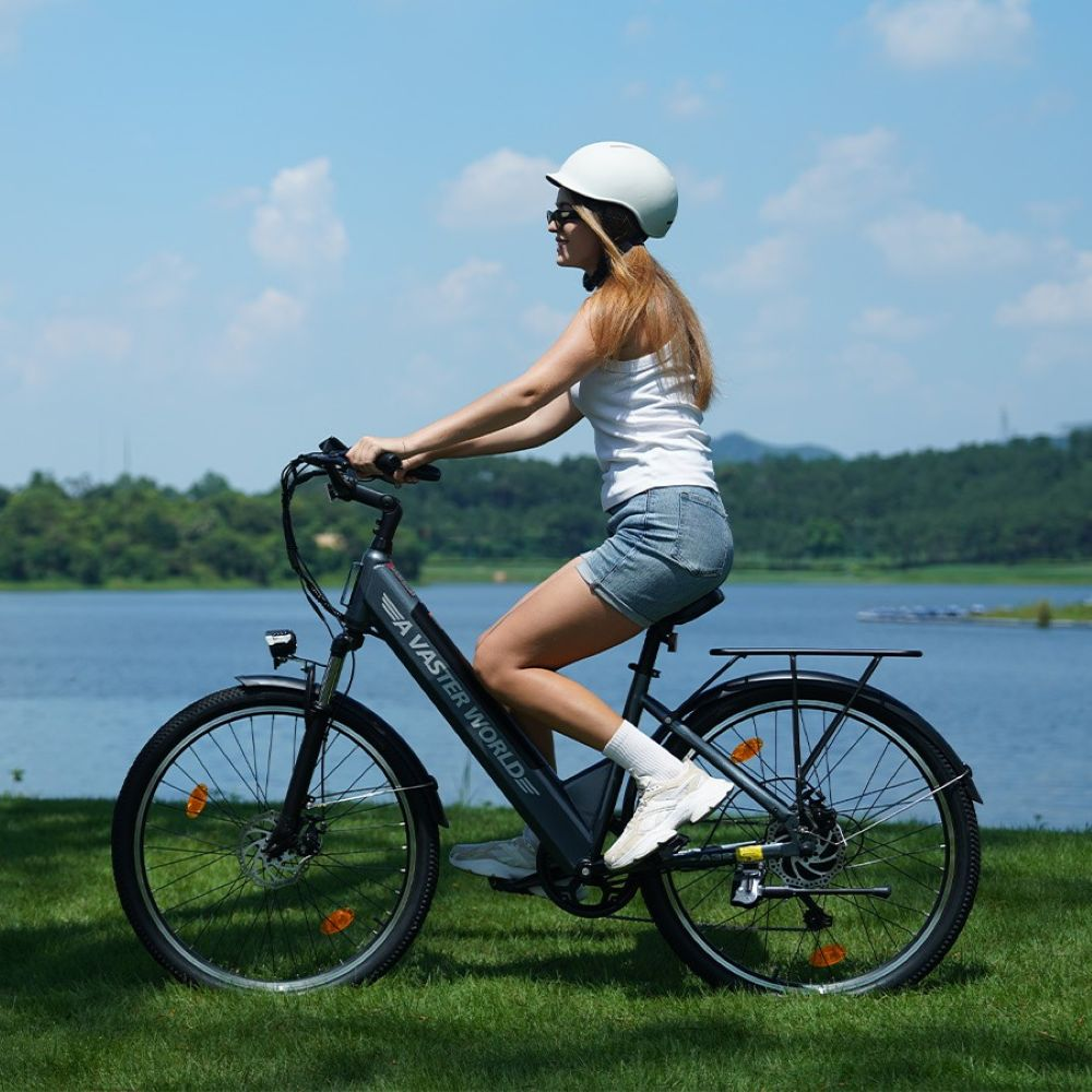 Una mujer con casco blanco y camiseta sin mangas monta en bicicleta eléctrica junto a un lago en un día soleado.