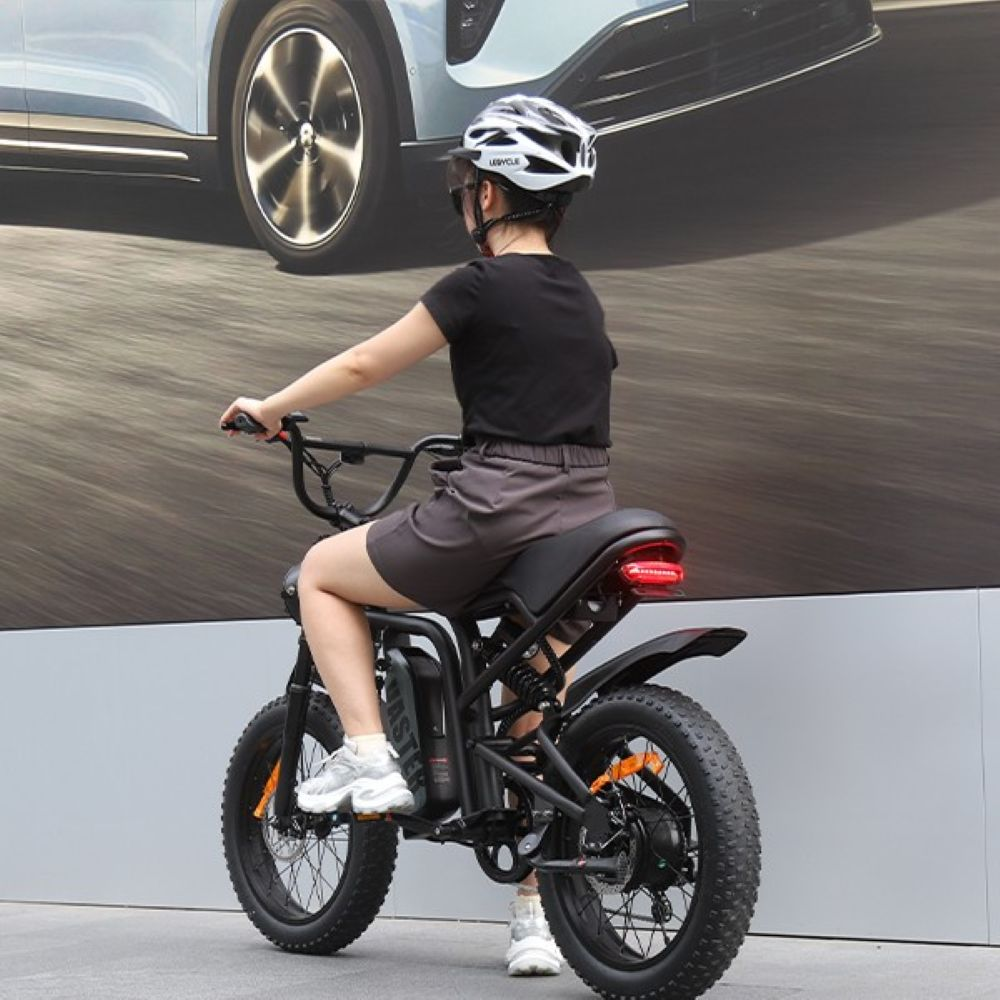 Persona con casco y camiseta negra sentada en una e-bike moderna frente a un gran cartel publicitario de coche.