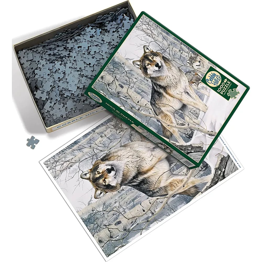 Ein offenes Puzzle und ein Plakat mit Wölfen im verschneiten Wald, dazu eine Schachtel voller Puzzleteile.