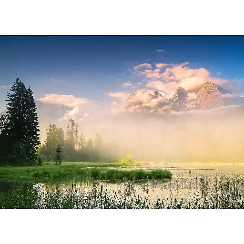 Ein alpiner See spiegelt hohe Kiefern, umgeben von Nebel und schneebedeckten Bergen unter einem blauen Himmel.