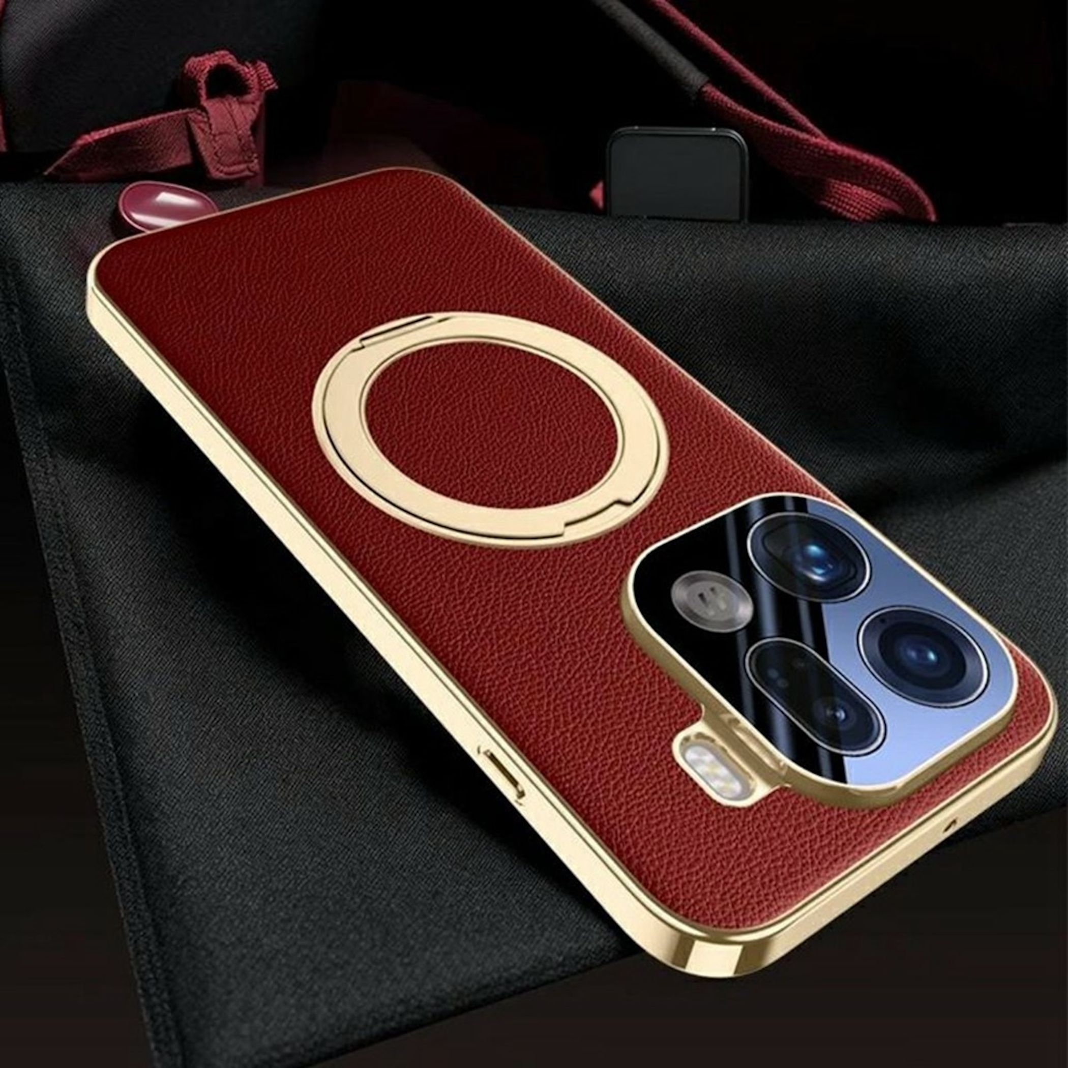 Ein rotes Leder-Smartphone-Case mit goldenen Akzenten, integriertem Ringstand und Kameraausschnitt auf schwarzem Stoff.