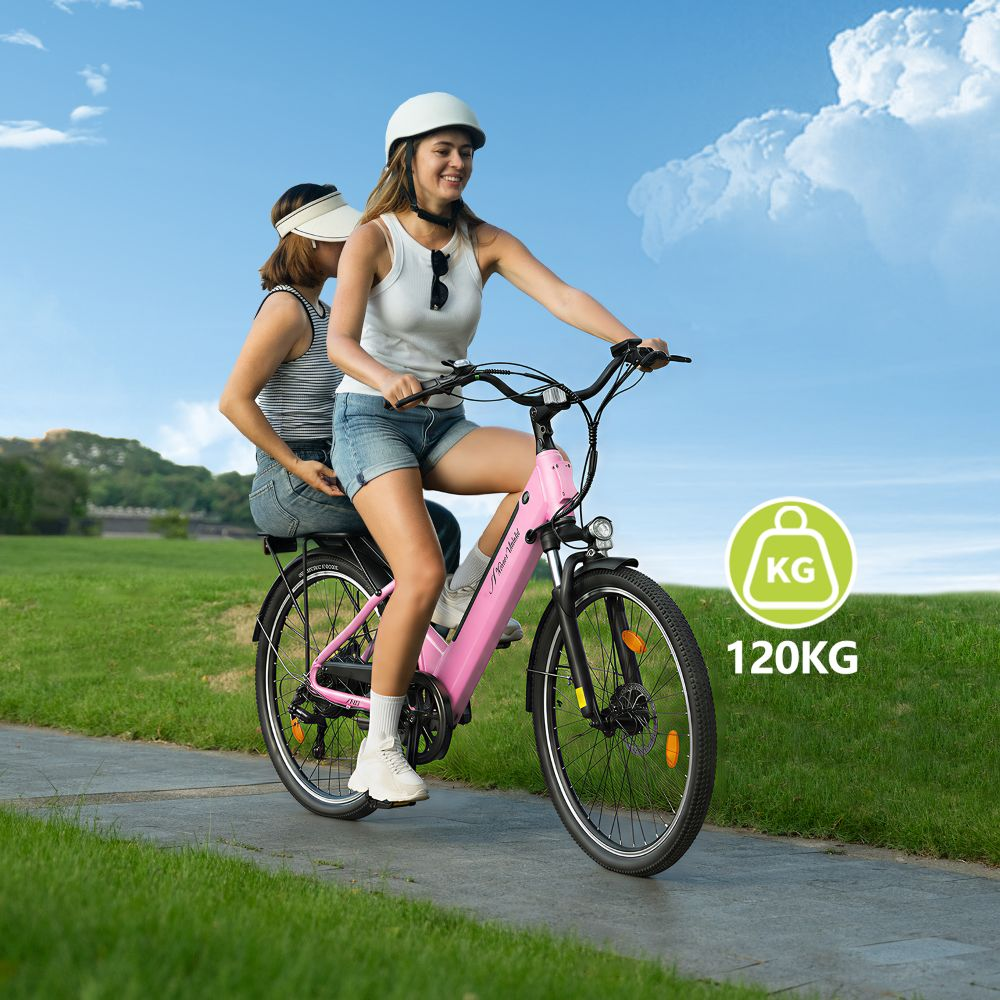 Dos mujeres montan en una bicicleta eléctrica rosa por un camino pavimentado con césped verde y cielo azul de fondo.