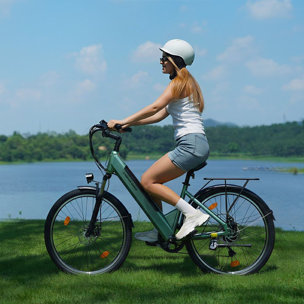 Una mujer con casco blanco monta en bicicleta eléctrica verde junto a un lago en un día soleado.