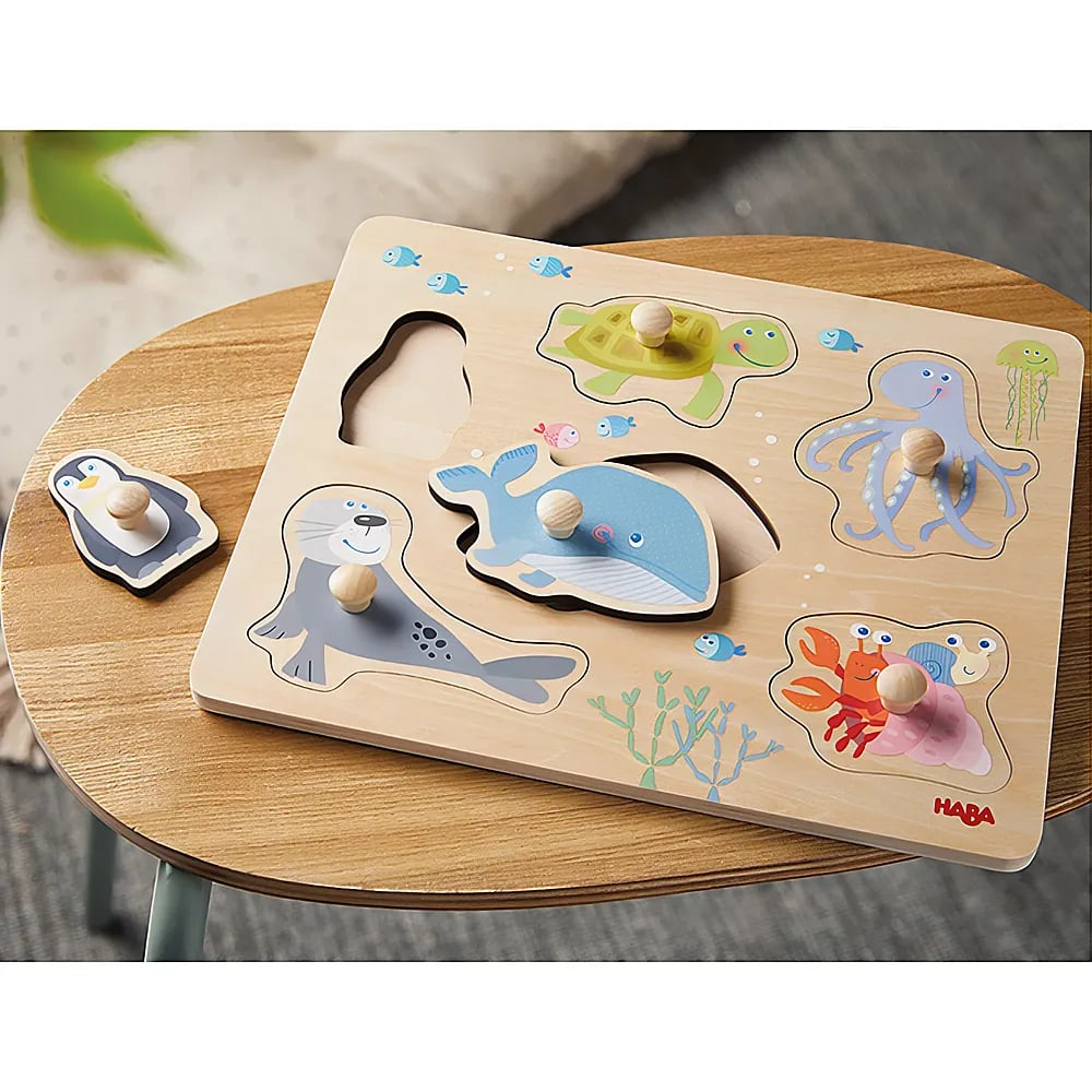 Ein Holz-Greifpuzzle auf einem Tisch mit Meerestieren und einer Pinguin-Figur daneben.