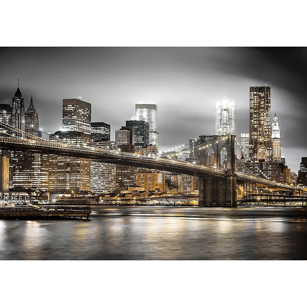 Night view of the illuminated Brooklyn Bridge against the New York City skyline over the river.