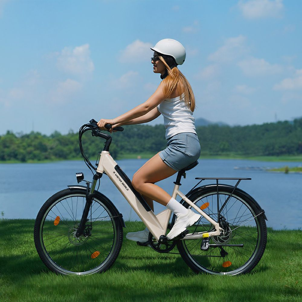 Una mujer rubia con casco monta en una bicicleta eléctrica beige junto al lago.