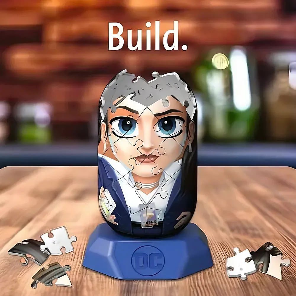 Ein zylindrisches Puzzle mit einem Frauengesicht steht auf einem blauen DC-Sockel, mit Puzzleteilen auf Holz.