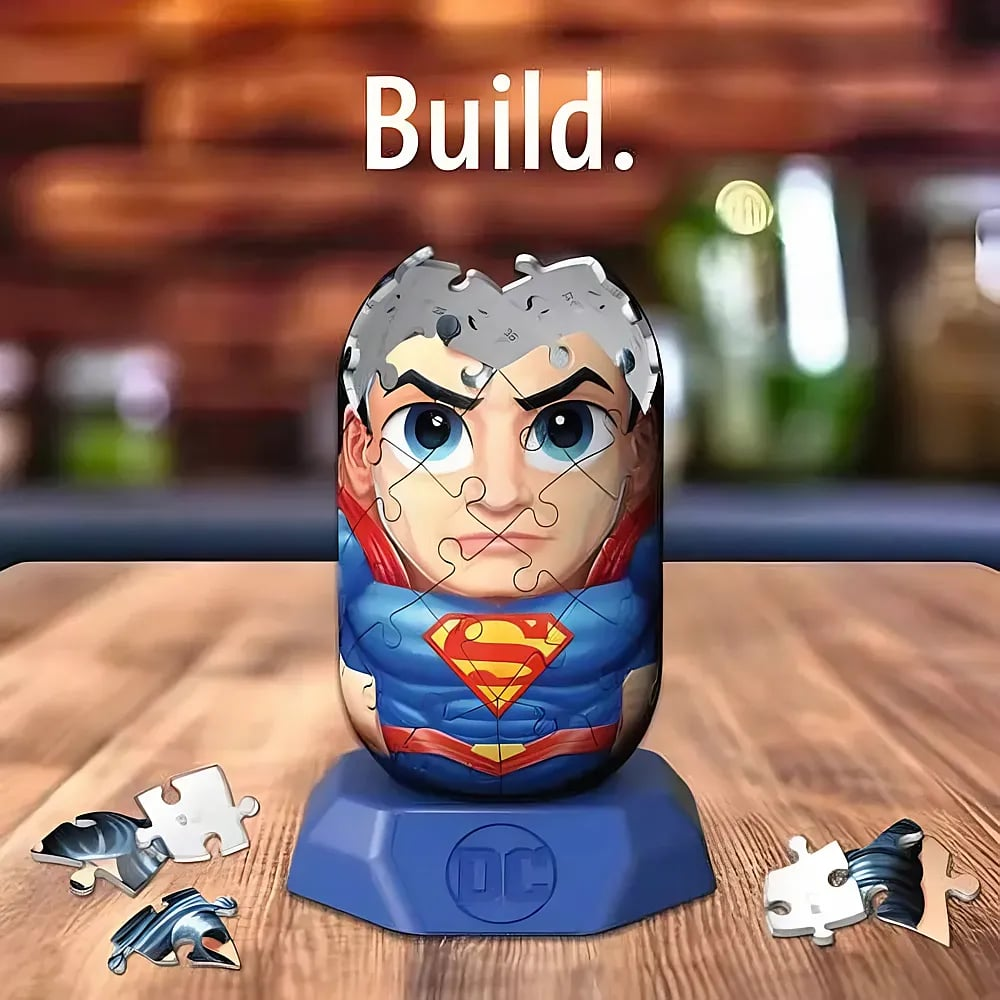 Ein Superman-3D-Puzzle auf einem blauen Sockel mit einigen losen Puzzleteilen auf einem Holztisch.