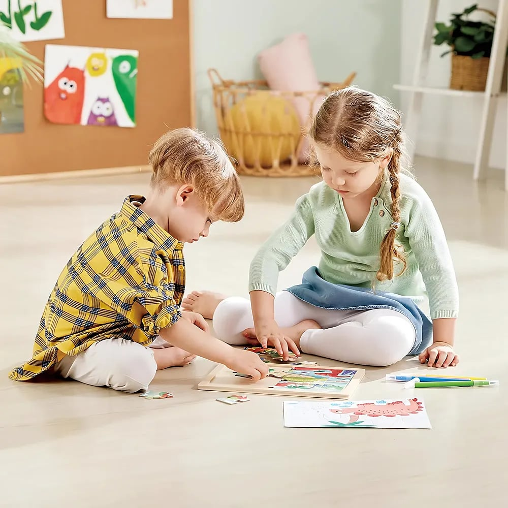 Zwei Kinder spielen auf dem Fußboden in einem hellen Zimmer mit einem Puzzle.