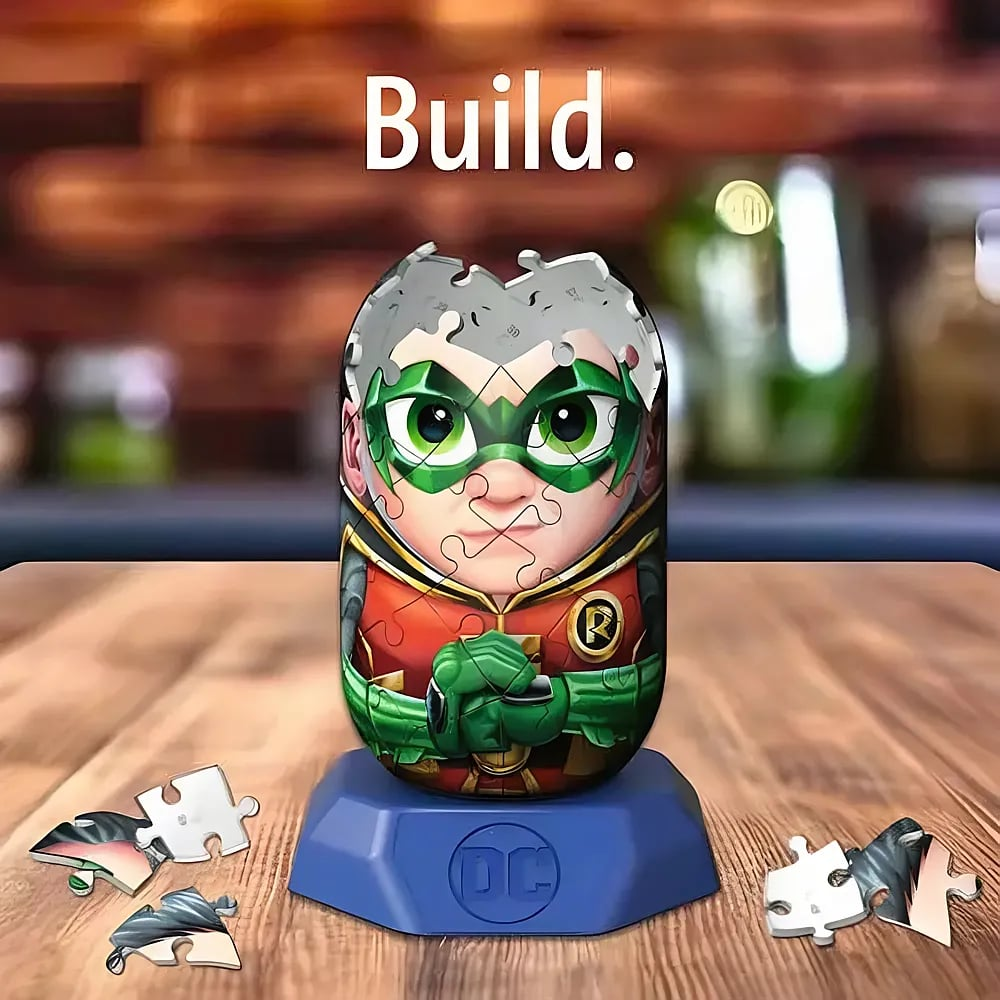 Ein Robin 3D-Puzzle auf einem blauen Sockel mit dem Aufdruck DC steht auf einem Holztisch, umgeben von losen Puzzleteilen.