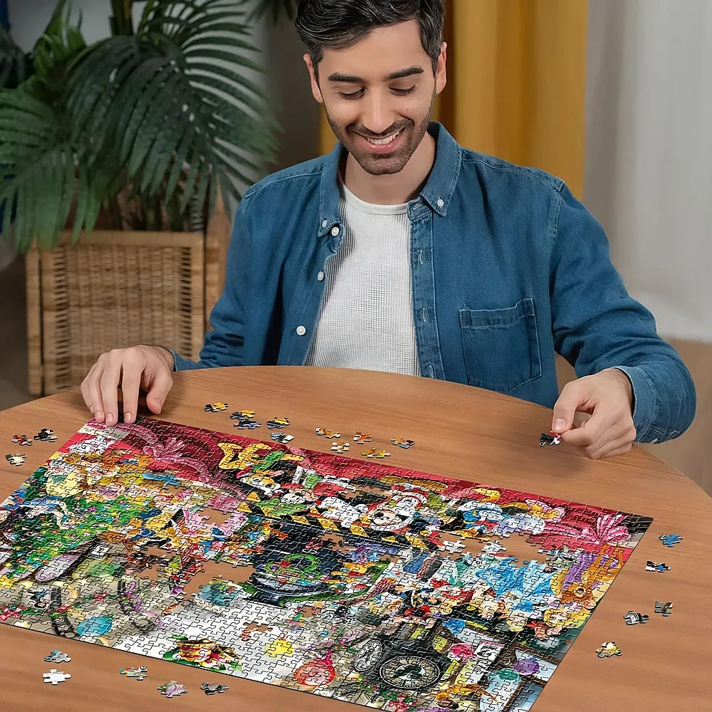 Ein lächelnder Mann sitzt an einem Holztisch und setzt ein großes, farbenfrohes Puzzle zusammen.