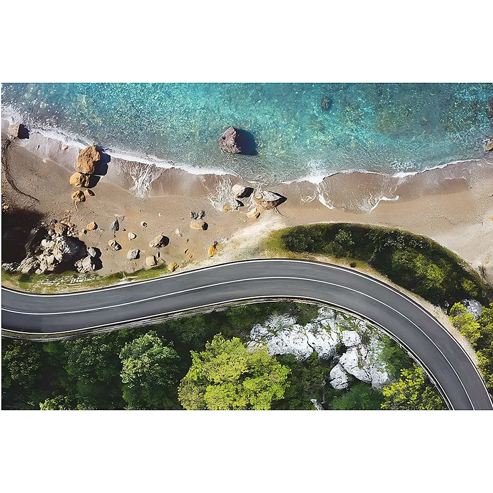 Luftaufnahme einer kurvigen Straße neben einem Sandstrand und klarem blauen Meer.