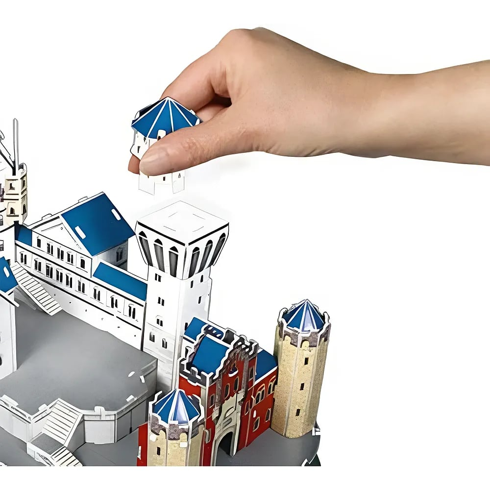 Eine Hand baut ein Papiermodell einer Burg mit blauem Dach und weißen Türmen zusammen.
