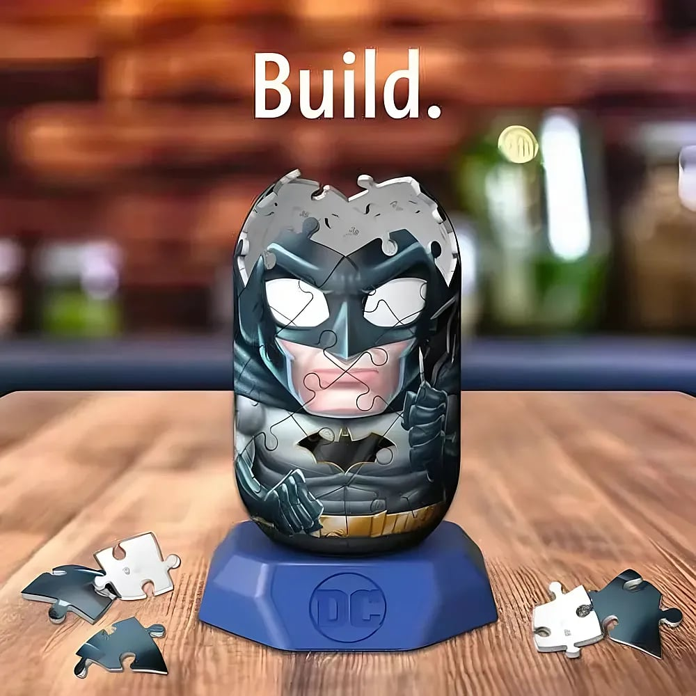 Ein zylindrisches Batman-Puzzle steht auf einem blauen DC-Sockel auf einem Holztisch, mit losen Puzzleteilen.