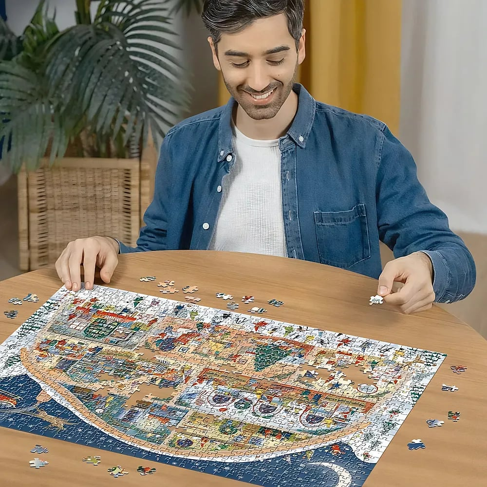 Ein lächelnder Mann in blauem Hemd sitzt an einem Holztisch und arbeitet an einem großen Puzzle.