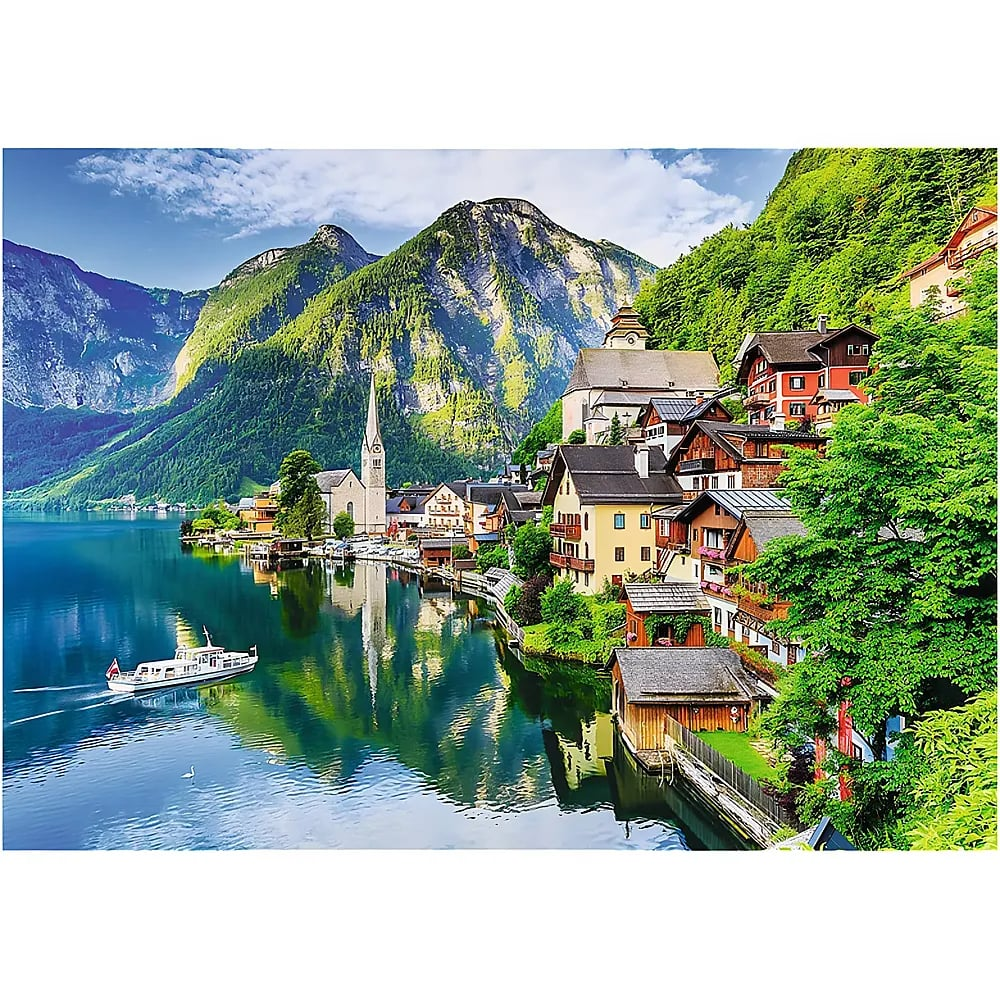 Scenic lakeside village with mountains, a church, and a boat on clear water under a cloudy sky.