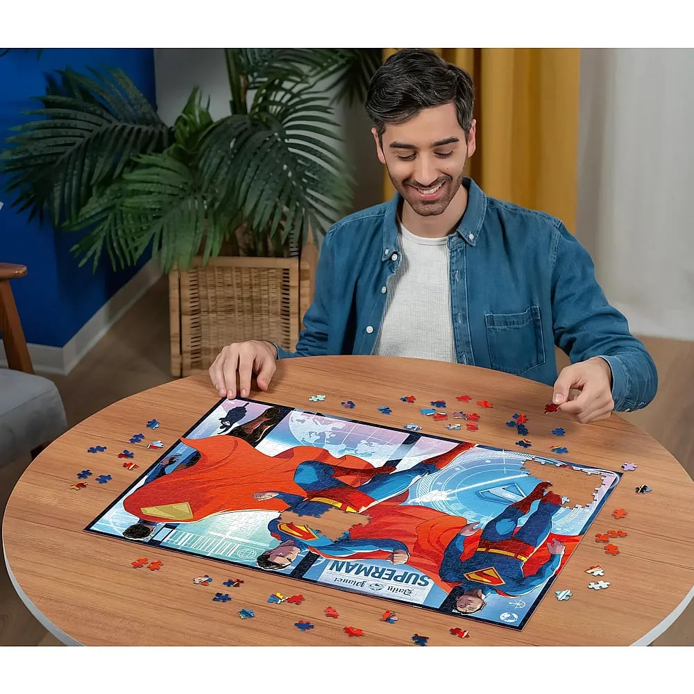 Mann mit blauem Hemd sitzt an einem Tisch und setzt ein Superman-Puzzle zusammen.